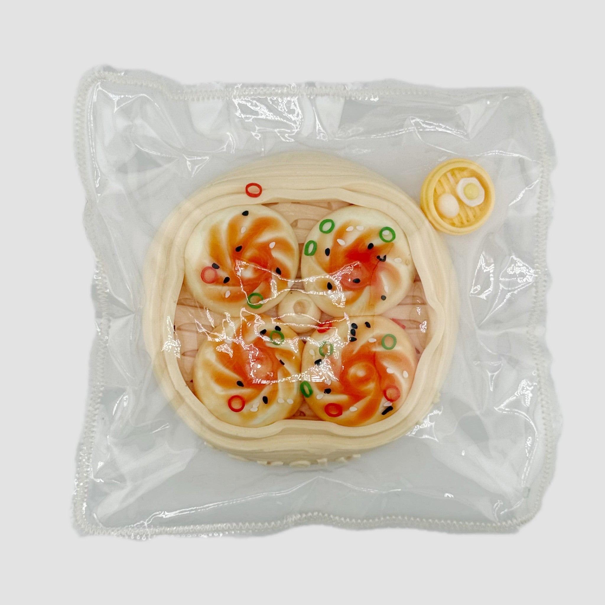 Dumpling squishy toy set packaged in a clear plastic bag, featuring a steamer basket design with four topped dumplings